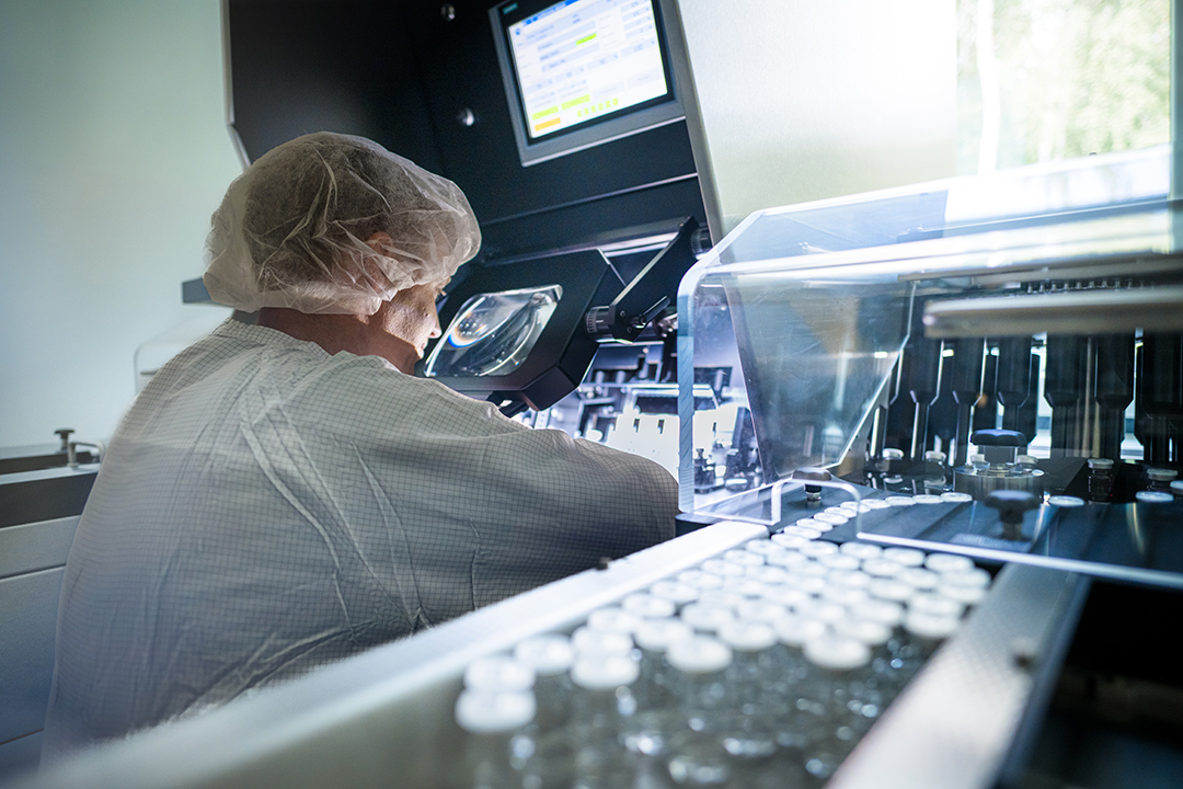 Cleanroom operator at an inspection machine visually checking vials for glass defects or impurities at ROTOP
