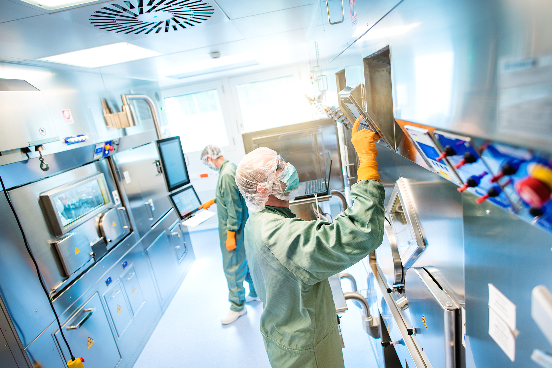 Two cleanroom operators in protective clothing operating the semi-automated production of radiopharmaceuticals for diagnostics and therapy
