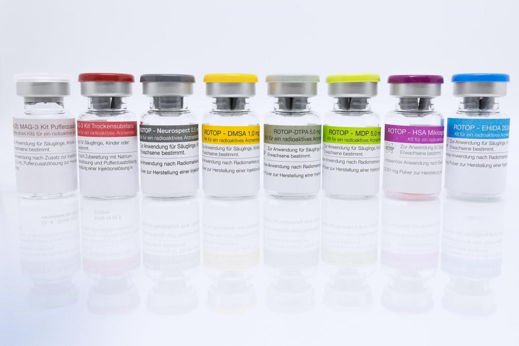 Eight ROTOP radiopharmaceutical kit vials with different colored caps, lined up on a reflective surface, used for preparation of injectable radiopharmaceuticals.
