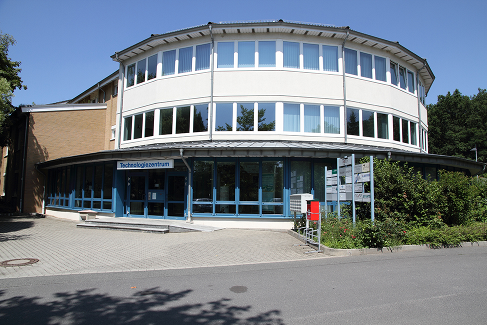 ROTOP Technology Center building with three floors, large windows, circular facade, blue-framed glass entrance, paved grounds, and surrounding greenery.